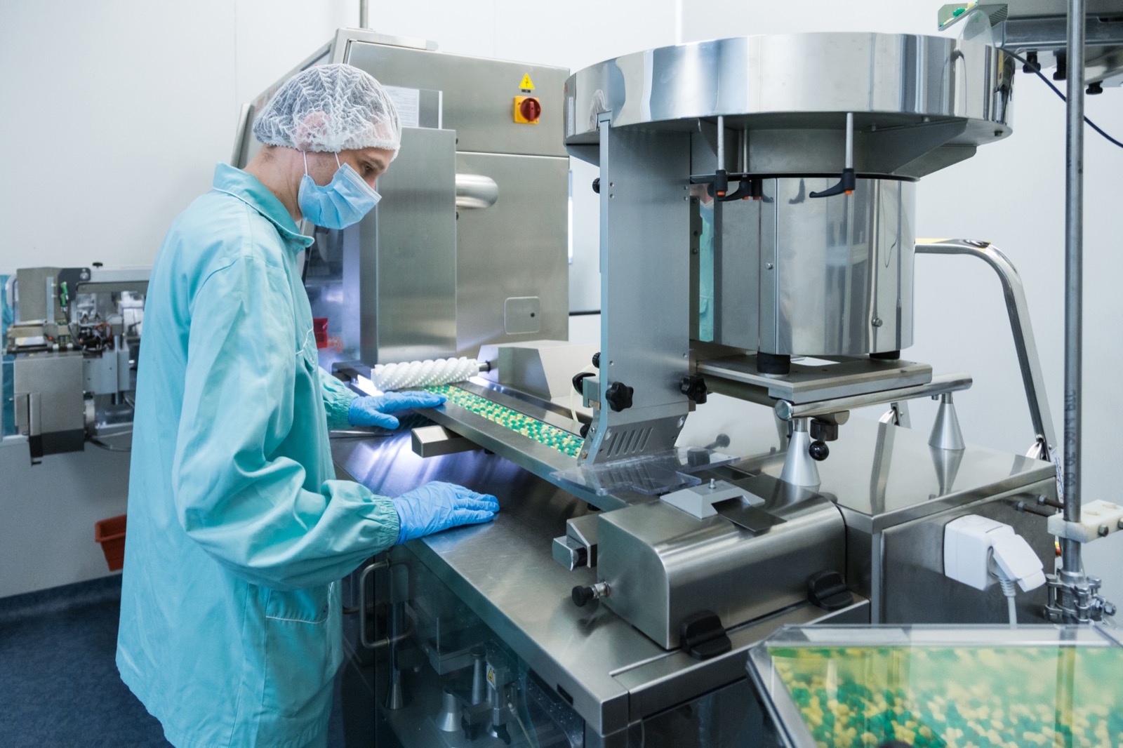 Pharmaceutical technician in sterile protective clothing operating a tablet production line